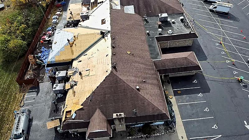 Aerial view of a commercial building mid roof tear-off, with old shingles removed and plywood roof decking exposed