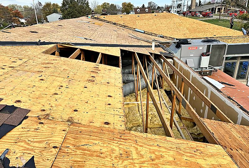 Roof deck during a tear-off with an open section showing insulation and ductwork next to a rooftop HVAC unit